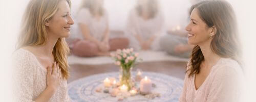 2 Frauen schauen sich an, eine hat ihre Hand auf dem Brustbereich liegen und ist gerührt