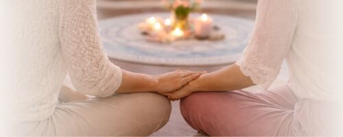 2 Frauen sitzen zum Kreis gewandt und eine legt ihre Hand auf die Hand der anderen Frau